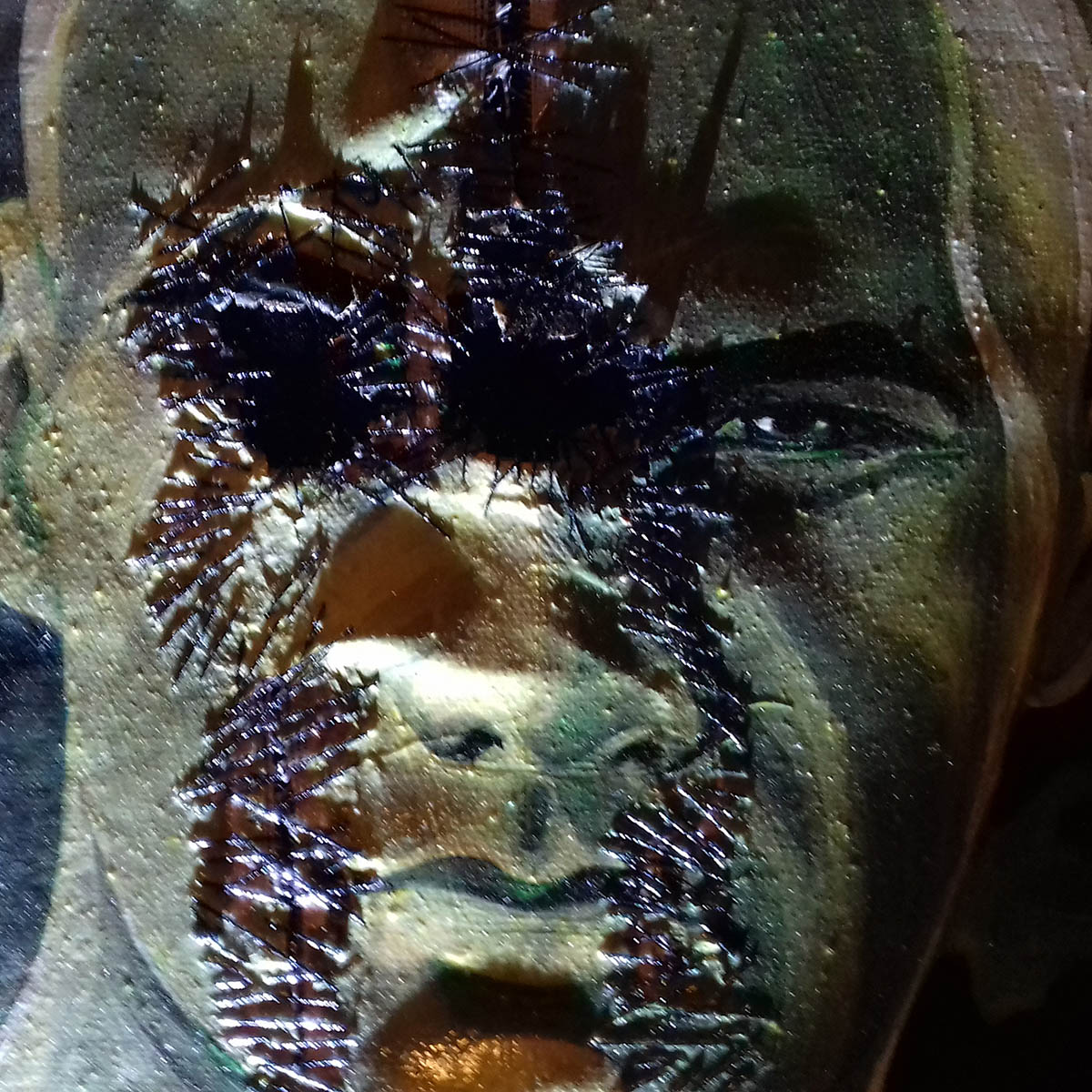 A mixed media artwork detail with dramatic lighting, showing a torn portrait of a masculine male figure, stitched with black thread onto a black canvas.